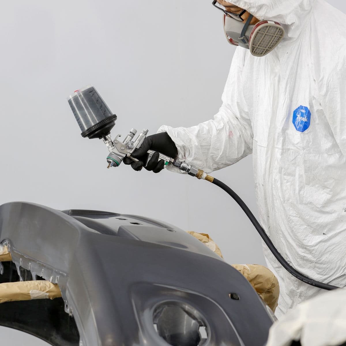 Technician in protective gear refinishing a bumper in the paint booth